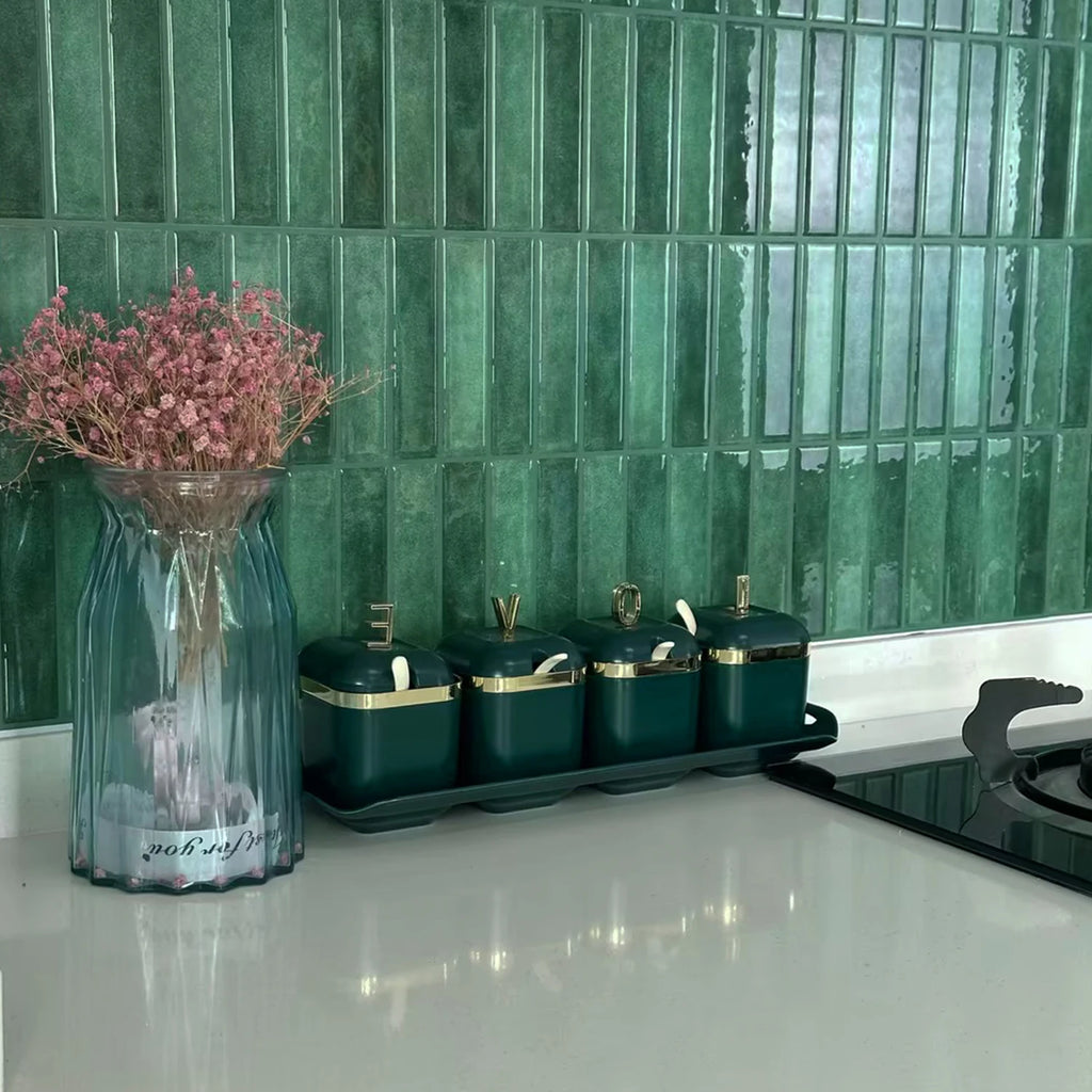 Green stacked tile backsplash on a kitchen counter with a glass vase of dried flowers and green canisters